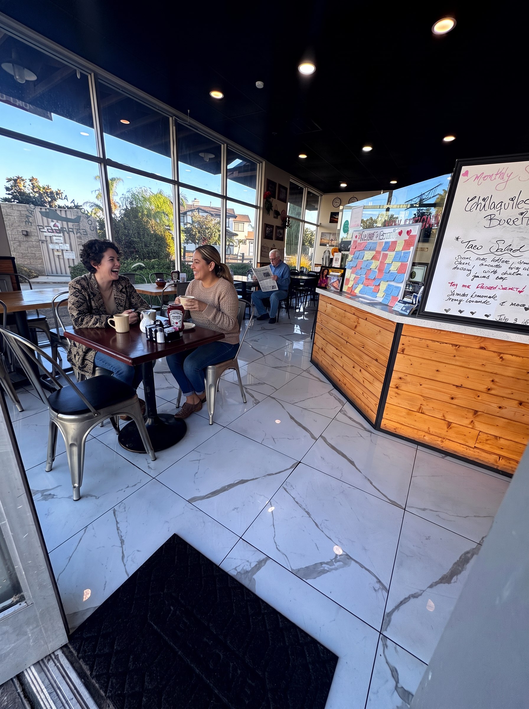 Two friends laughing over coffee at a window table on a quiet morning